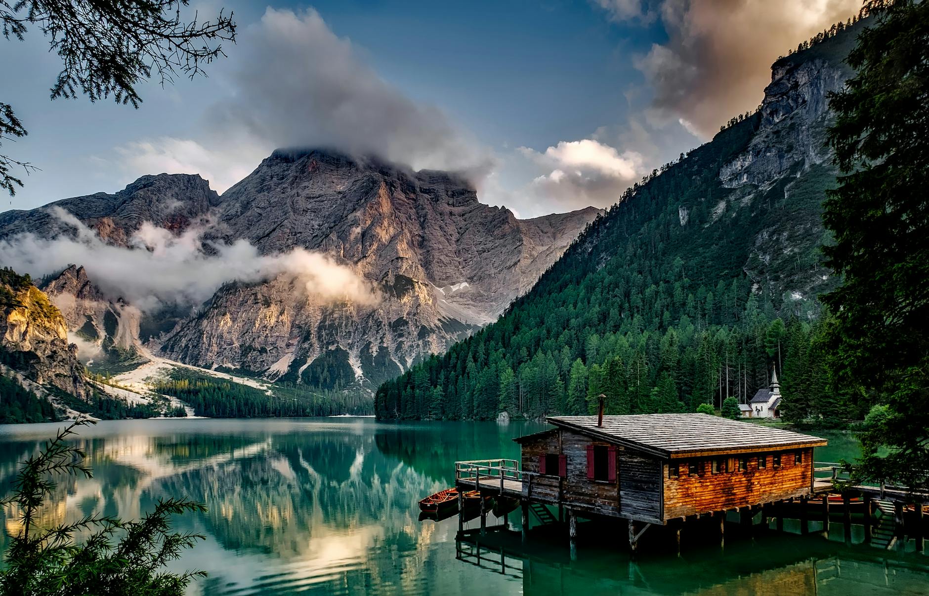 mirror lake reflecting wooden house in middle of lake overlooking mountain ranges