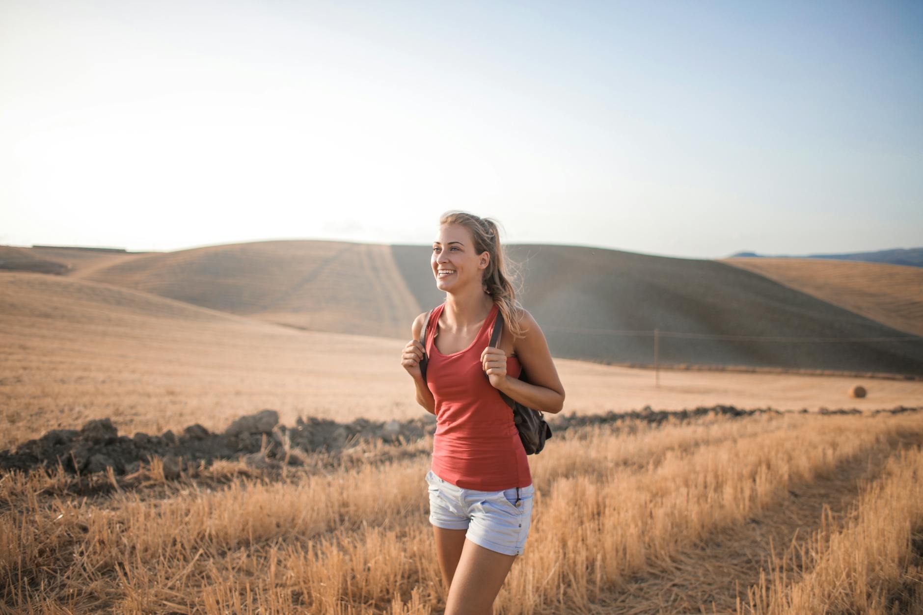 woman in red tank top and blue shorts standing on brown grass field